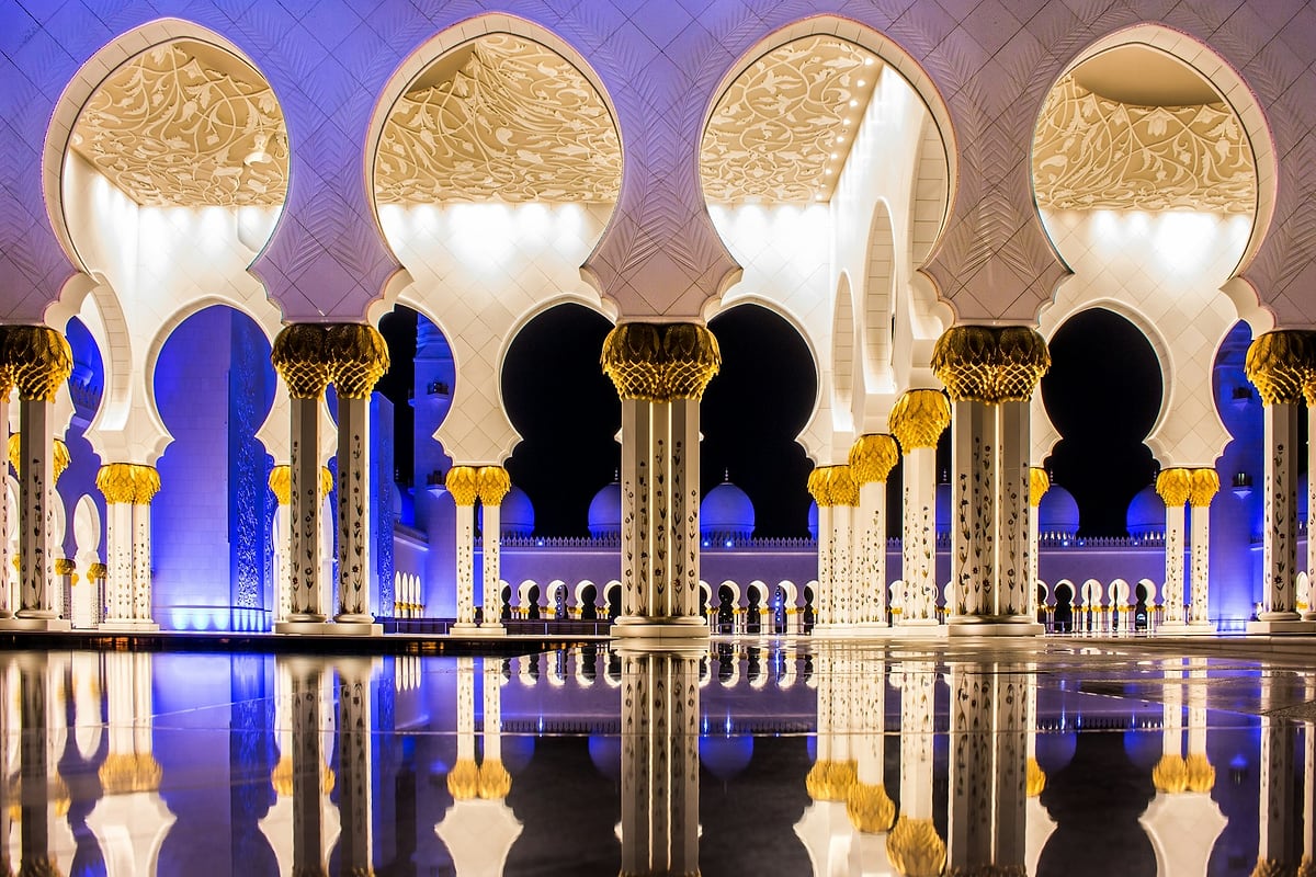 أروقة جامع الشيخ زايد الكبير المضاءة ليلًا وانعكاسها على أحواض الماء