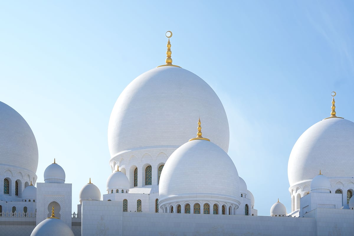 The white domes of Sheikh Zayed Grand Mosque against a clear blue sky